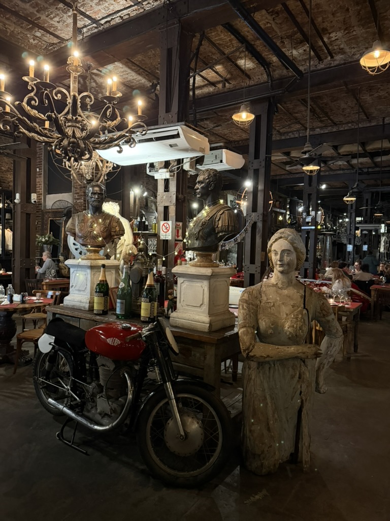 Motocicleta antigua, esculturas y lámparas dentro de Nápoles Bar