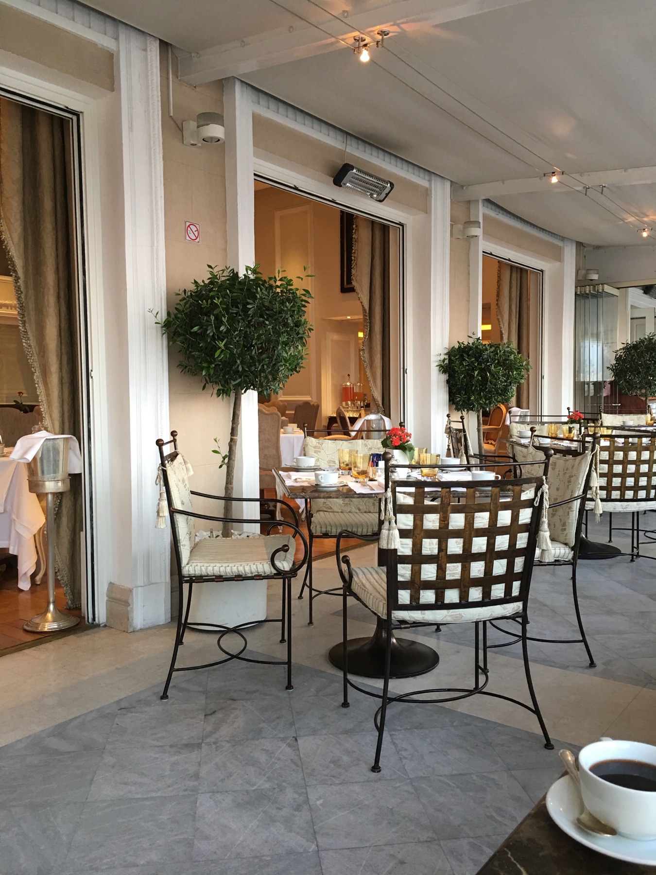 Terraza del desayuno del King George en Atenas, con mesas preparadas y una taza de café
