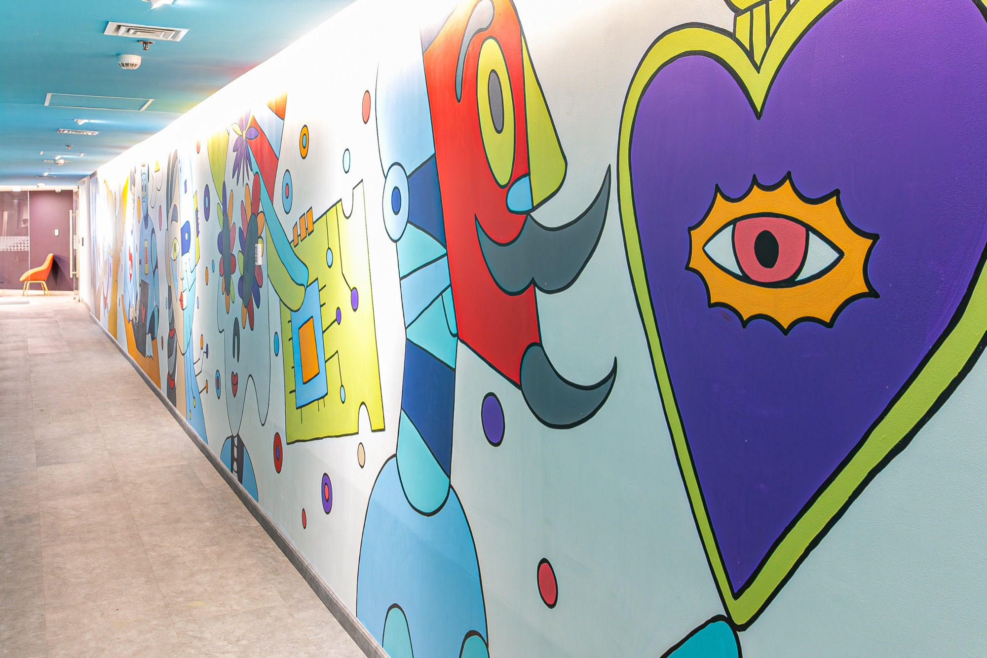 Mural terminado de Cocolvú a lo largo del corredor, con figuras de colores y un corazón violeta en primer plano
