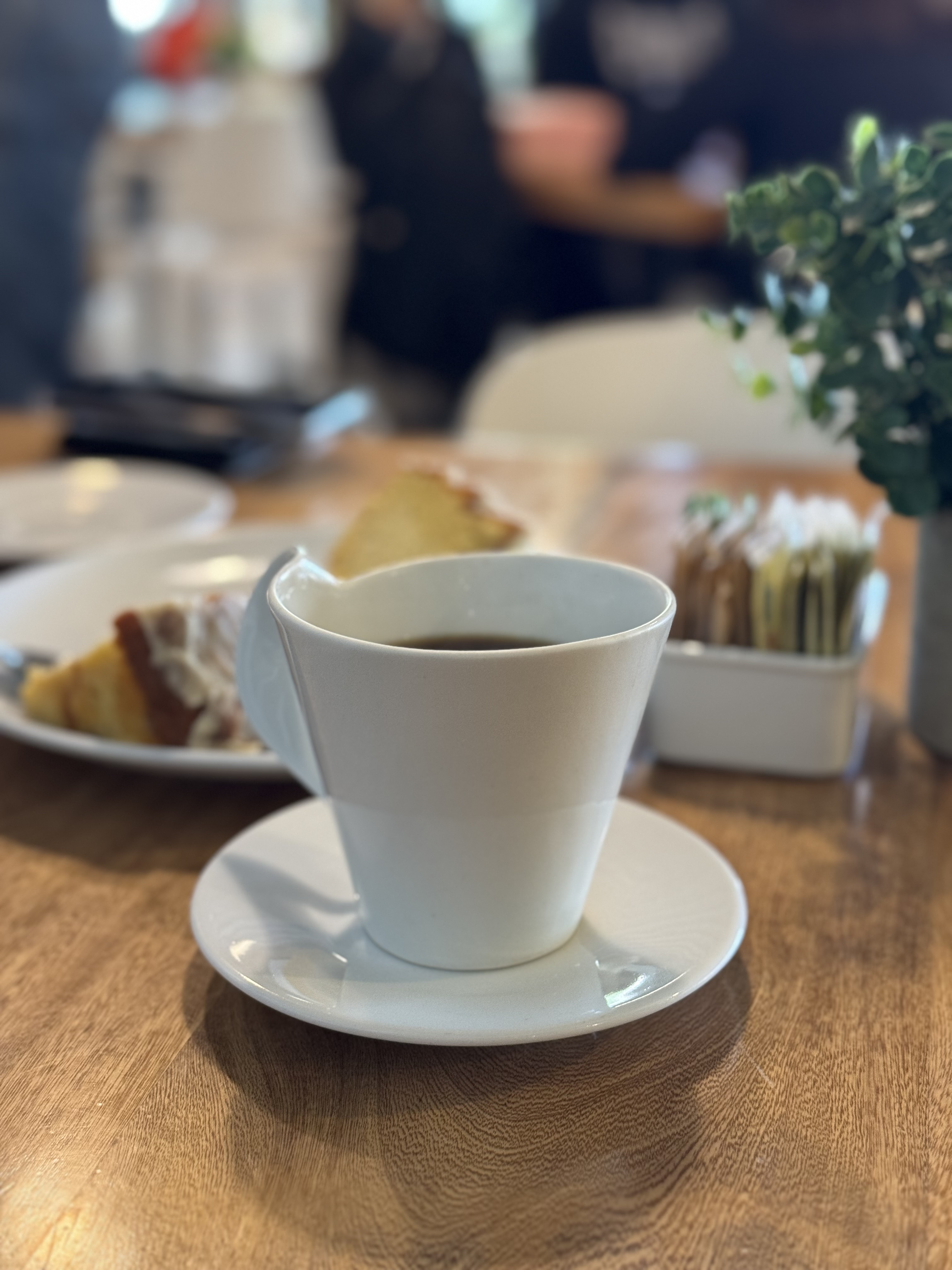 Una taza de café sobre una mesa, con el ambiente de la cafetería al fondo