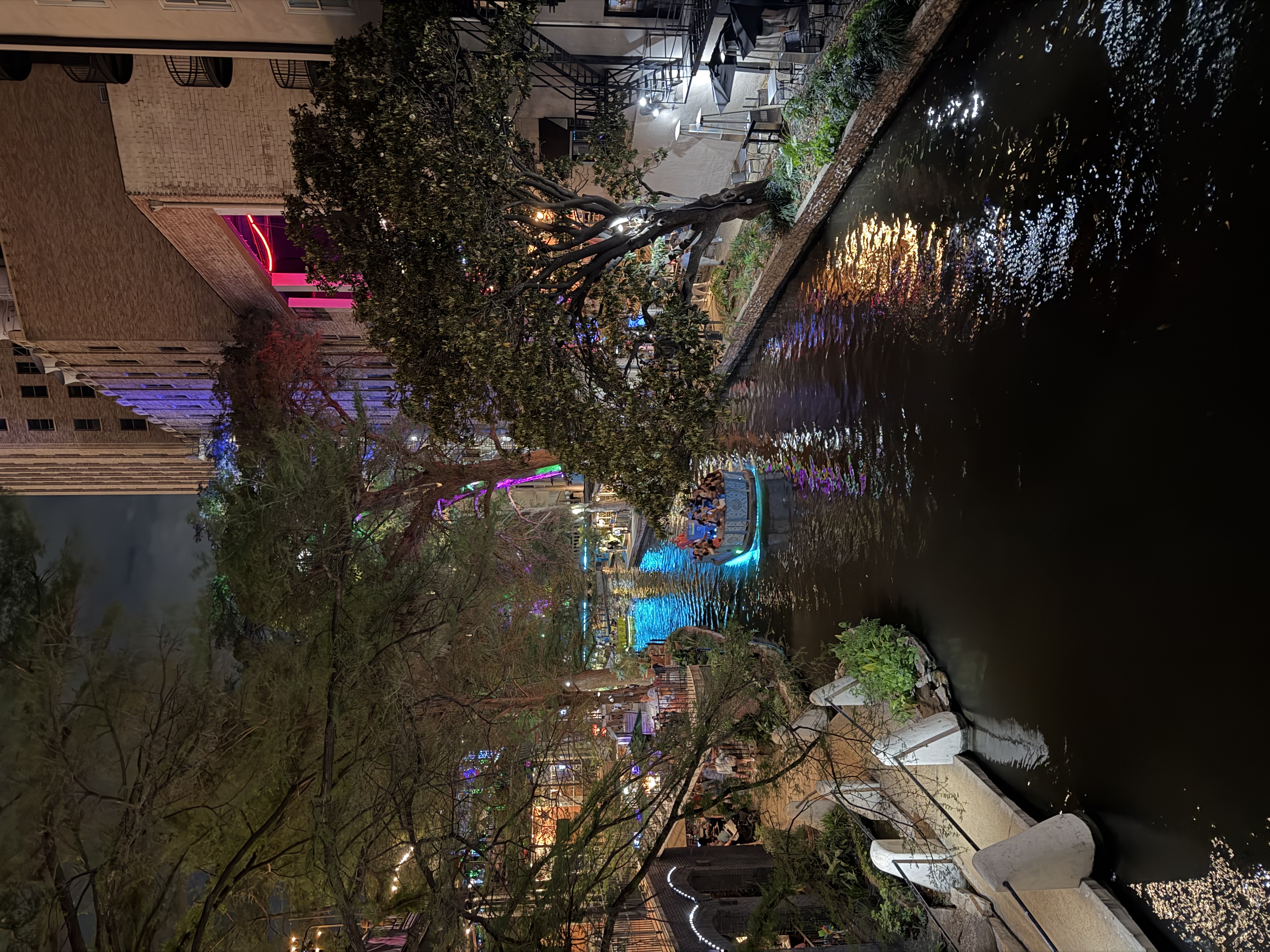 Bote navegando por el River Walk iluminado por la noche