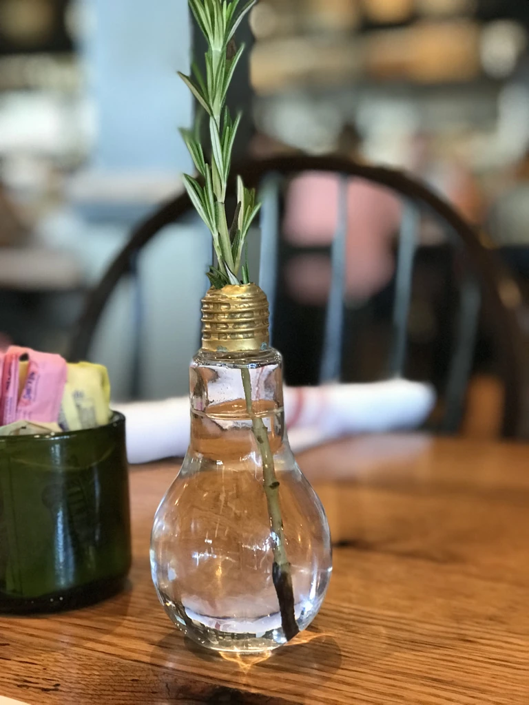 Un recipiente de vidrio con forma de bombilla y una rama verde sobre una mesa de madera en Whiskey Cake.