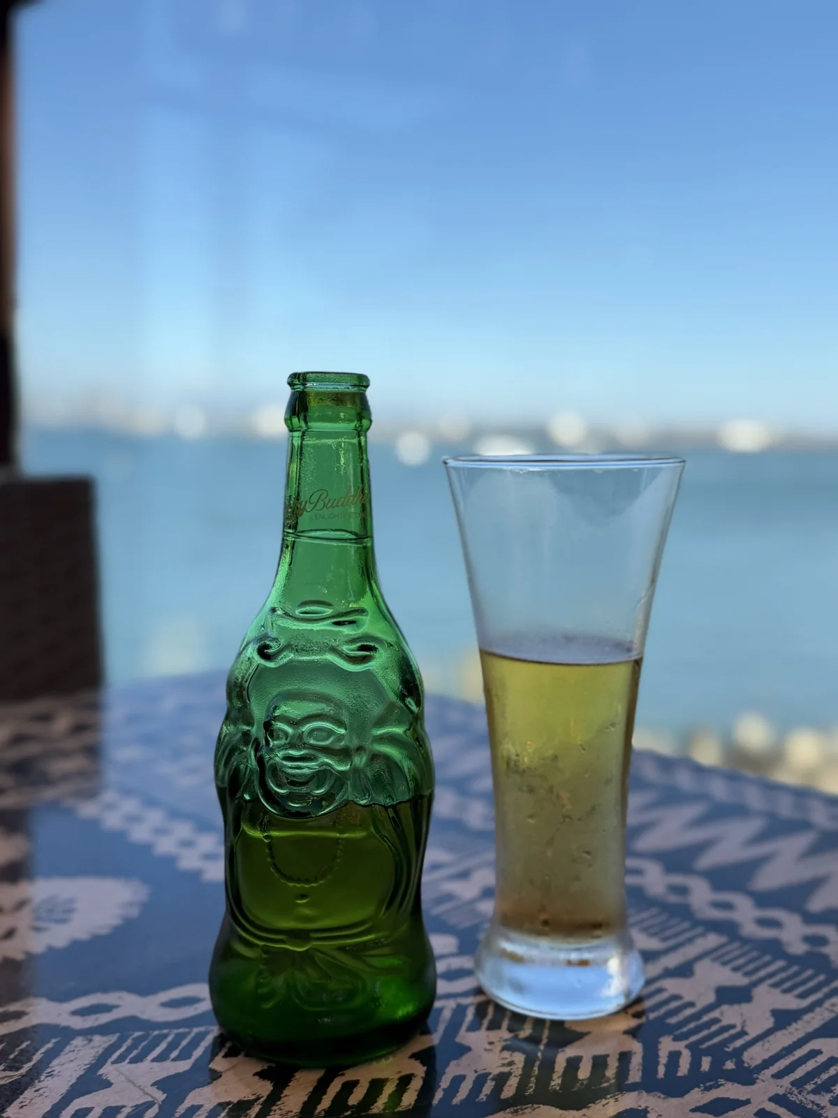 Una botella verde de cerveza y un vaso sobre la mesa de Bali Hai, con la bahía desenfocada al fondo.