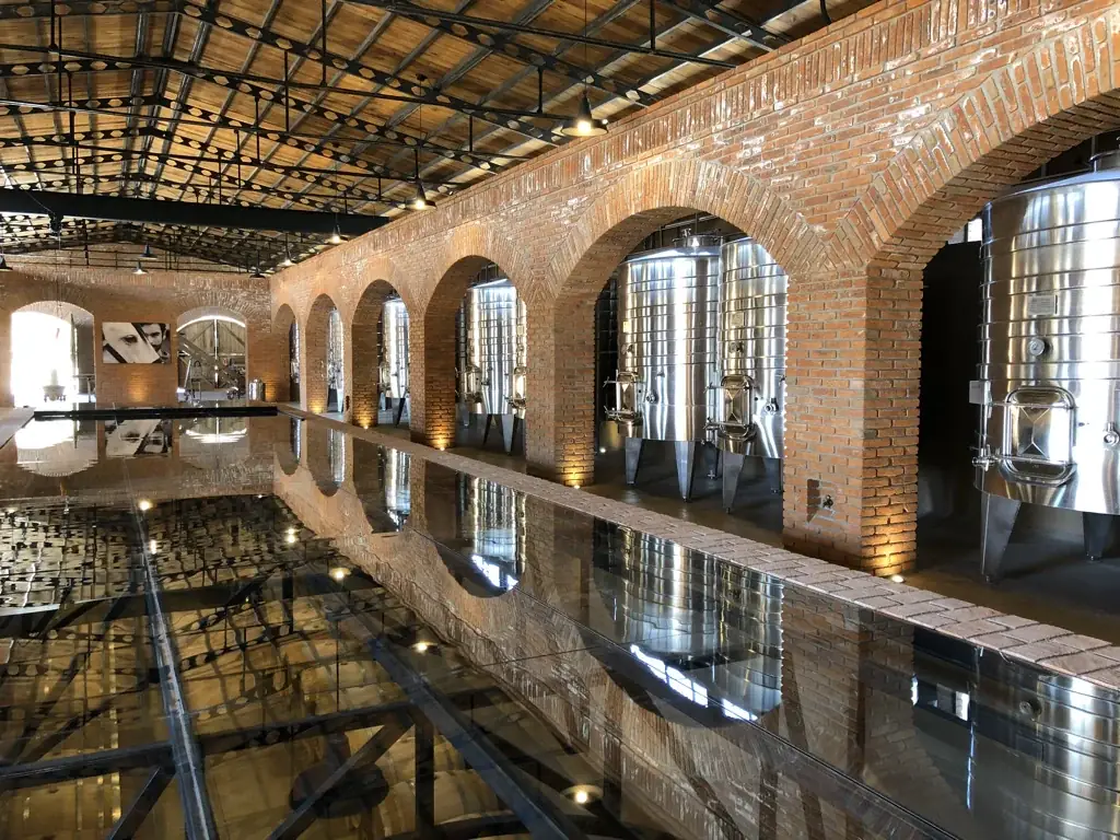 Tanques de acero entre arcos de ladrillo y reflejos en el interior de la bodega