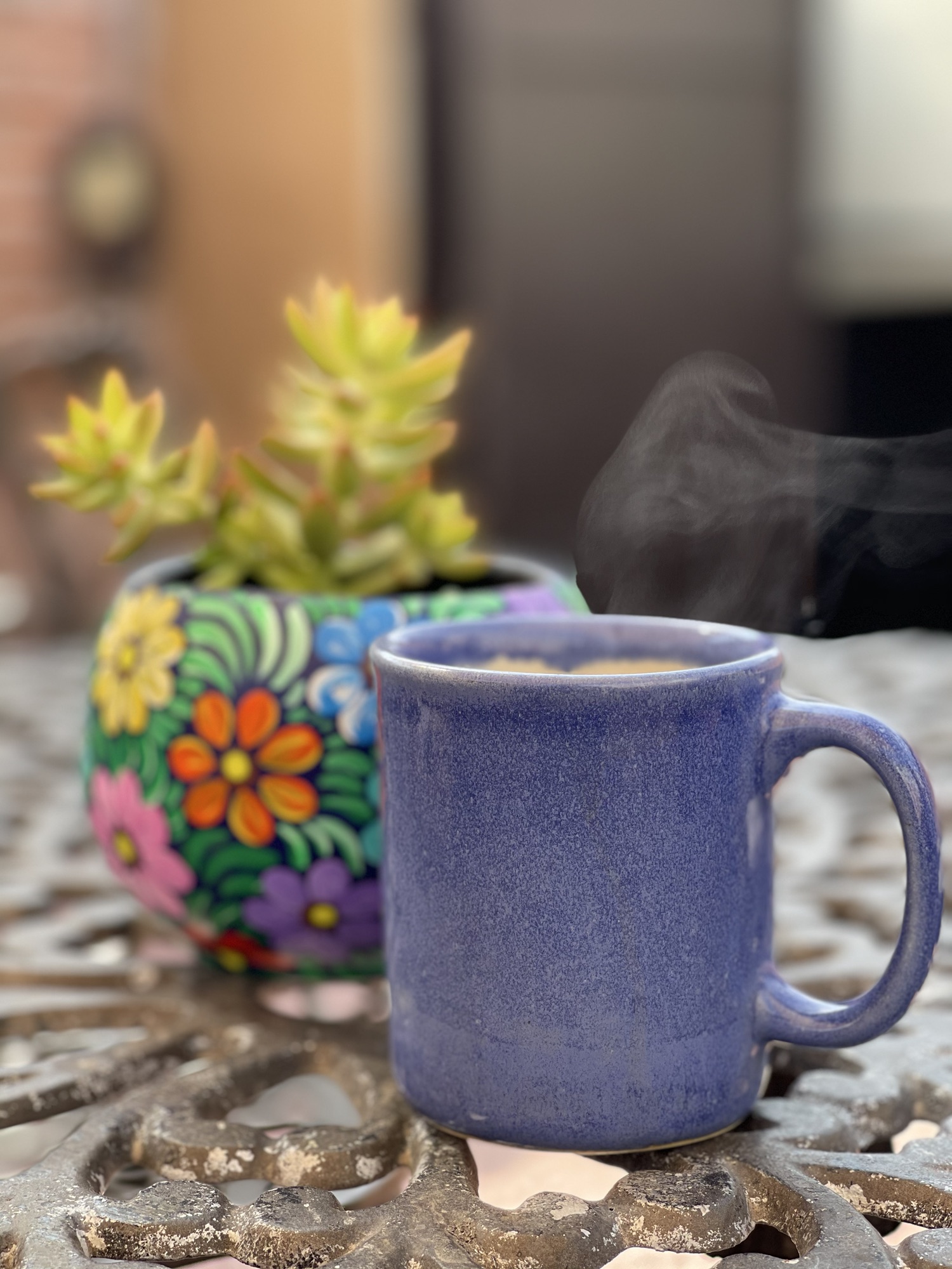 Taza de café caliente junto a una maceta artesanal colorida
